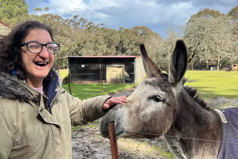 Happy woman with disability patting a donkey and smiling at camera