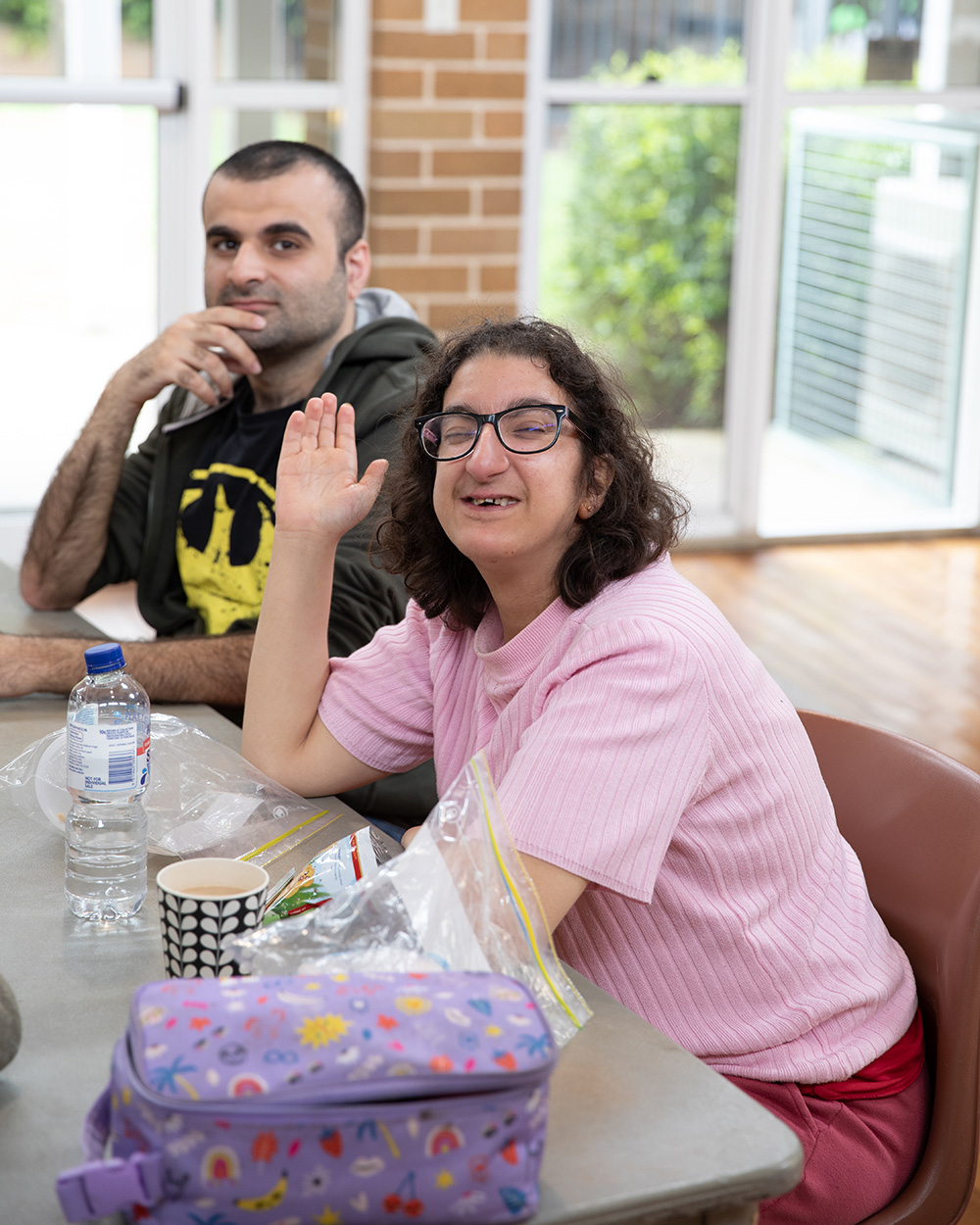 At Divine Care Australia, our journey began with a deeply personal experience that ignited a passion for making a difference. Two disabled friends smiling happily at camera while sitting at table